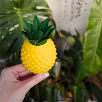 D printed pineapple watering spike held in hand in front of indoor houseplants