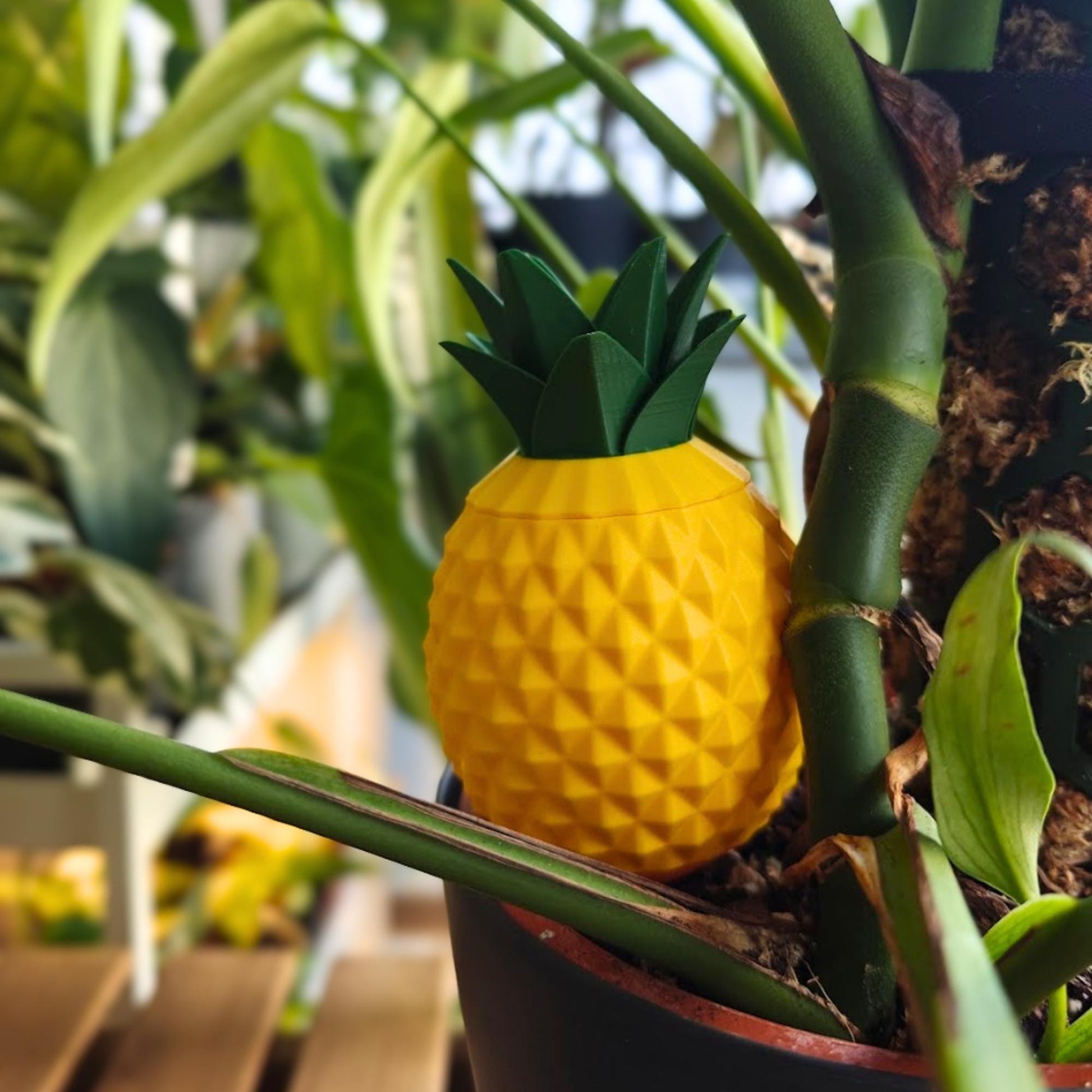 Pineapple-shaped 3D printed watering spike placed in a plant pot among green houseplant leaves.