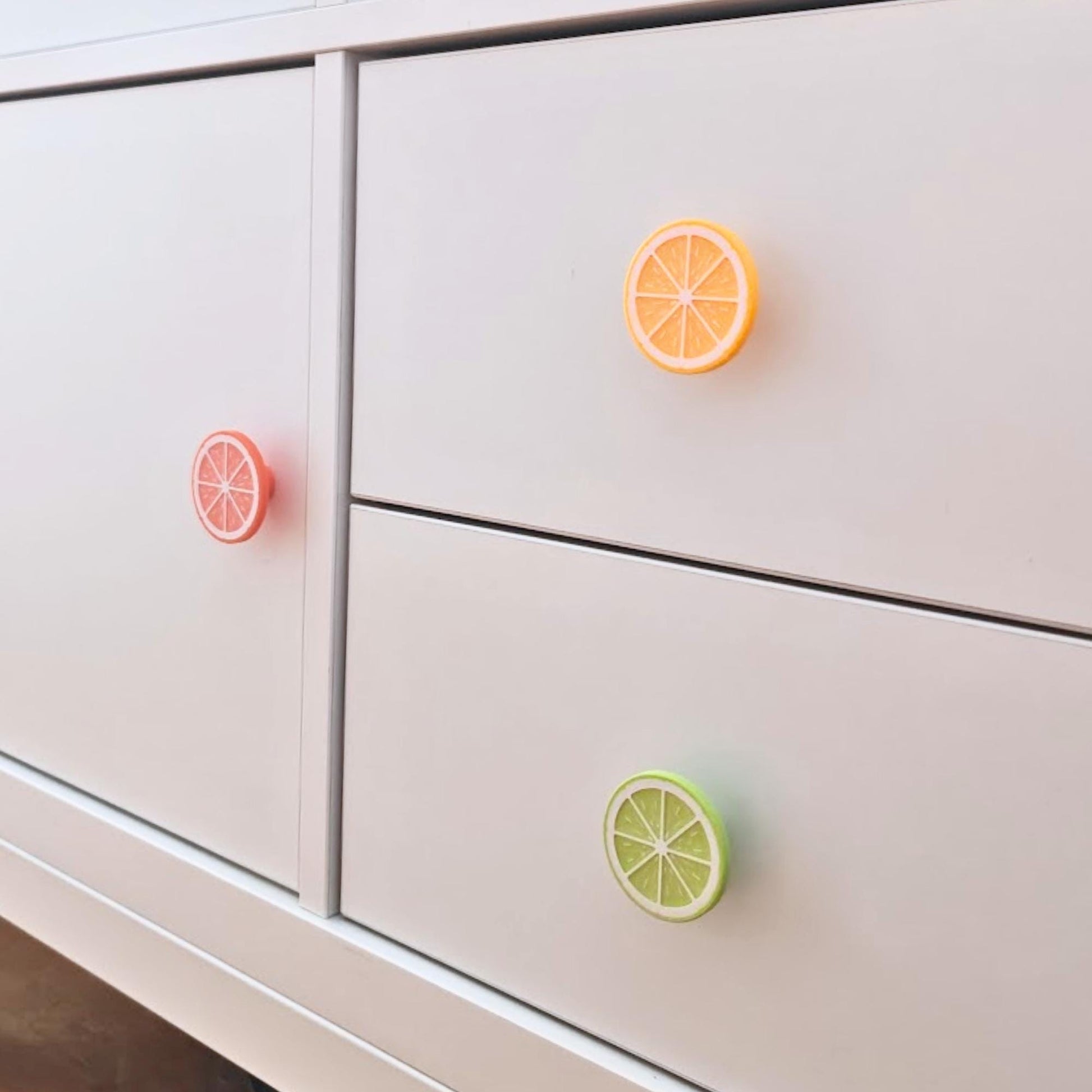 Citrus slice knobs installed on a white dresser, showing lemon, orange, and lime cabinet pull designs.