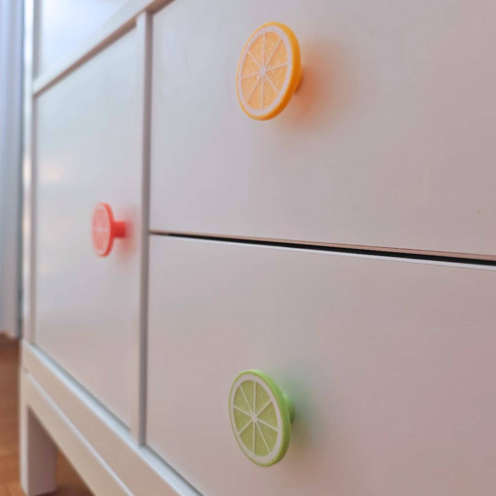 Close-up of citrus fruit slice drawer knobs on a white cabinet, showing colorful lemon, orange, and lime designs.