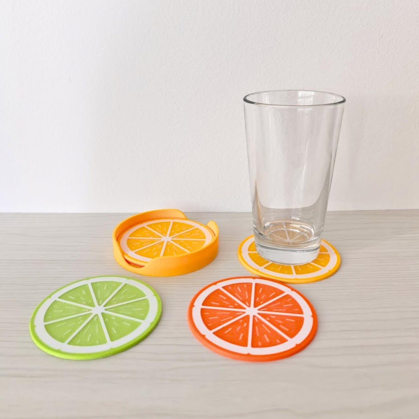 Citrus coasters displayed with a glass on one coaster and additional lemon, lime and orange coasters on the table.