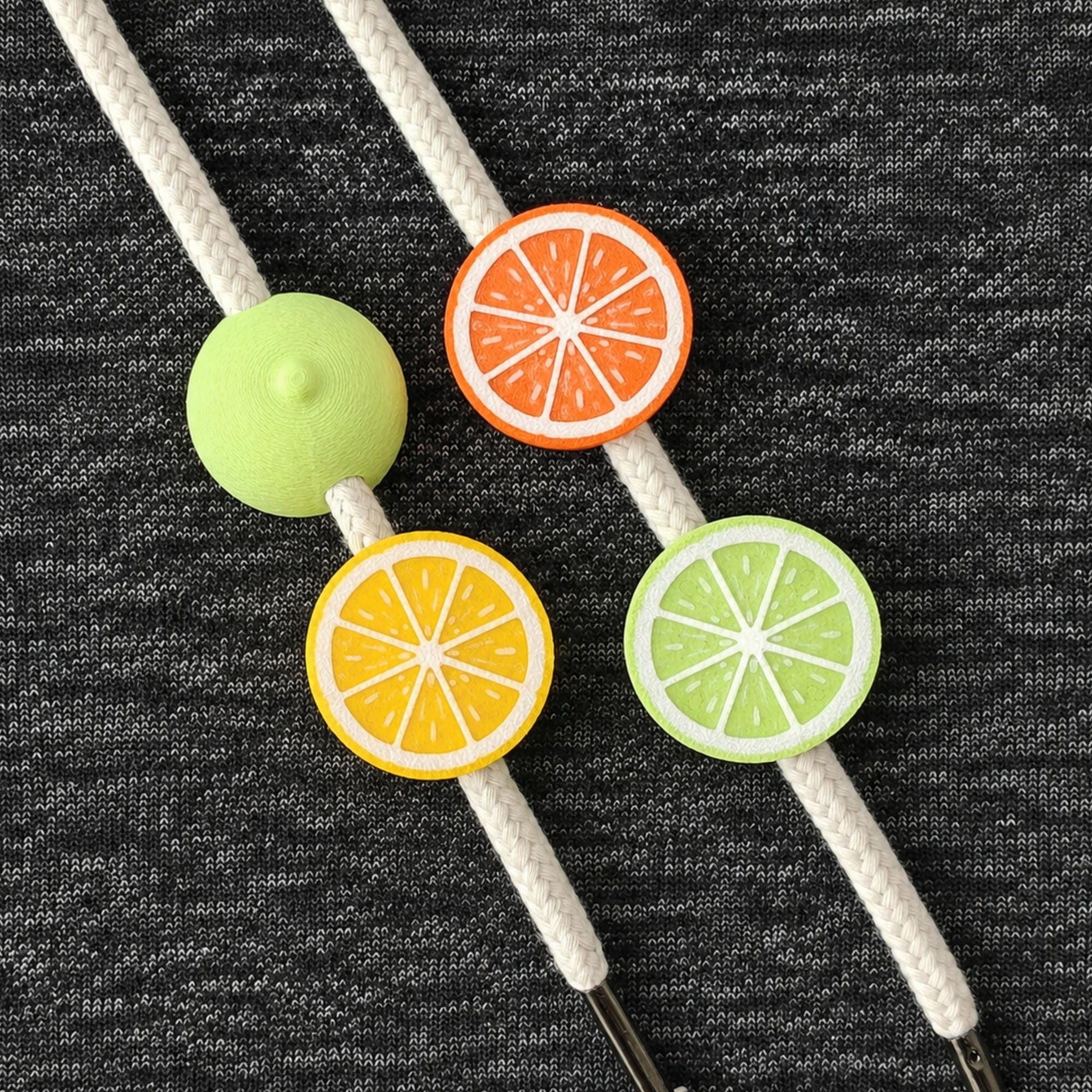 Mixed citrus drawstring charm set with lemon, orange, lime and round beads on white hoodie cords.