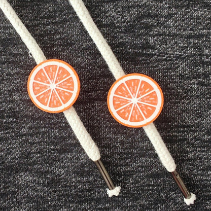 Orange half-fruit drawstring charms on white hoodie cords, close-up view against dark gray fabric.