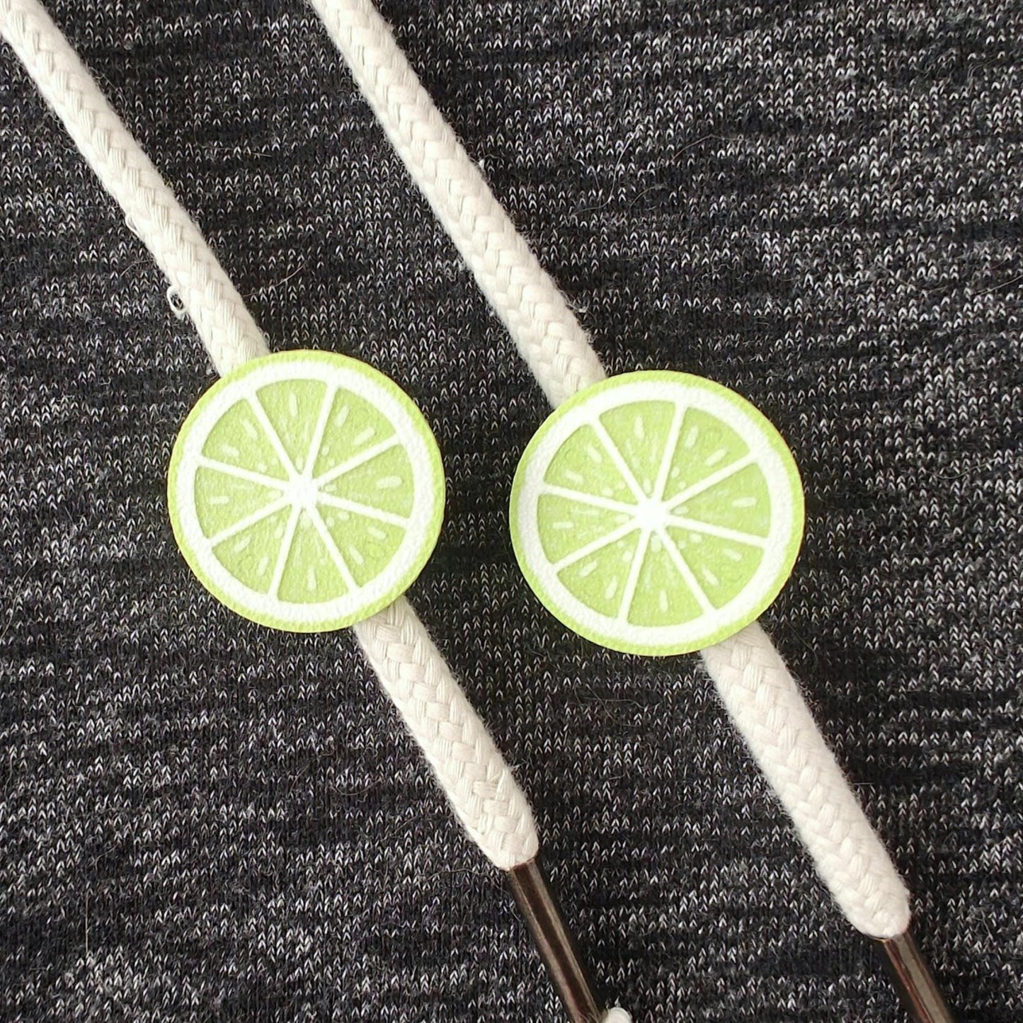 Lime green half-fruit drawstring charms on white hoodie cords, close-up view on dark gray fabric.