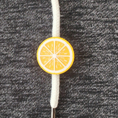 Yellow lemon half-fruit drawstring charm on white hoodie cord, close-up view on dark gray fabric.