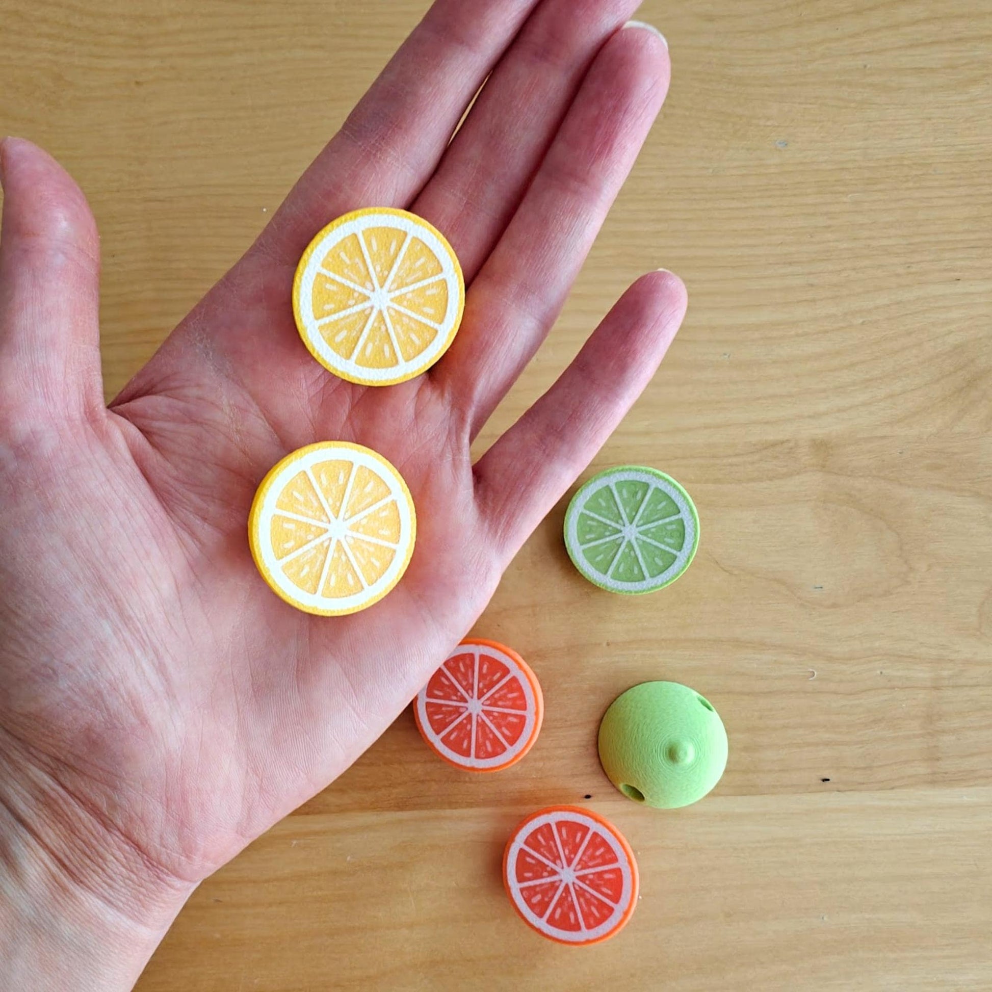 Citrus hoodie beads and half-fruit charms displayed in hand, showing lemon, orange, lime and green designs.