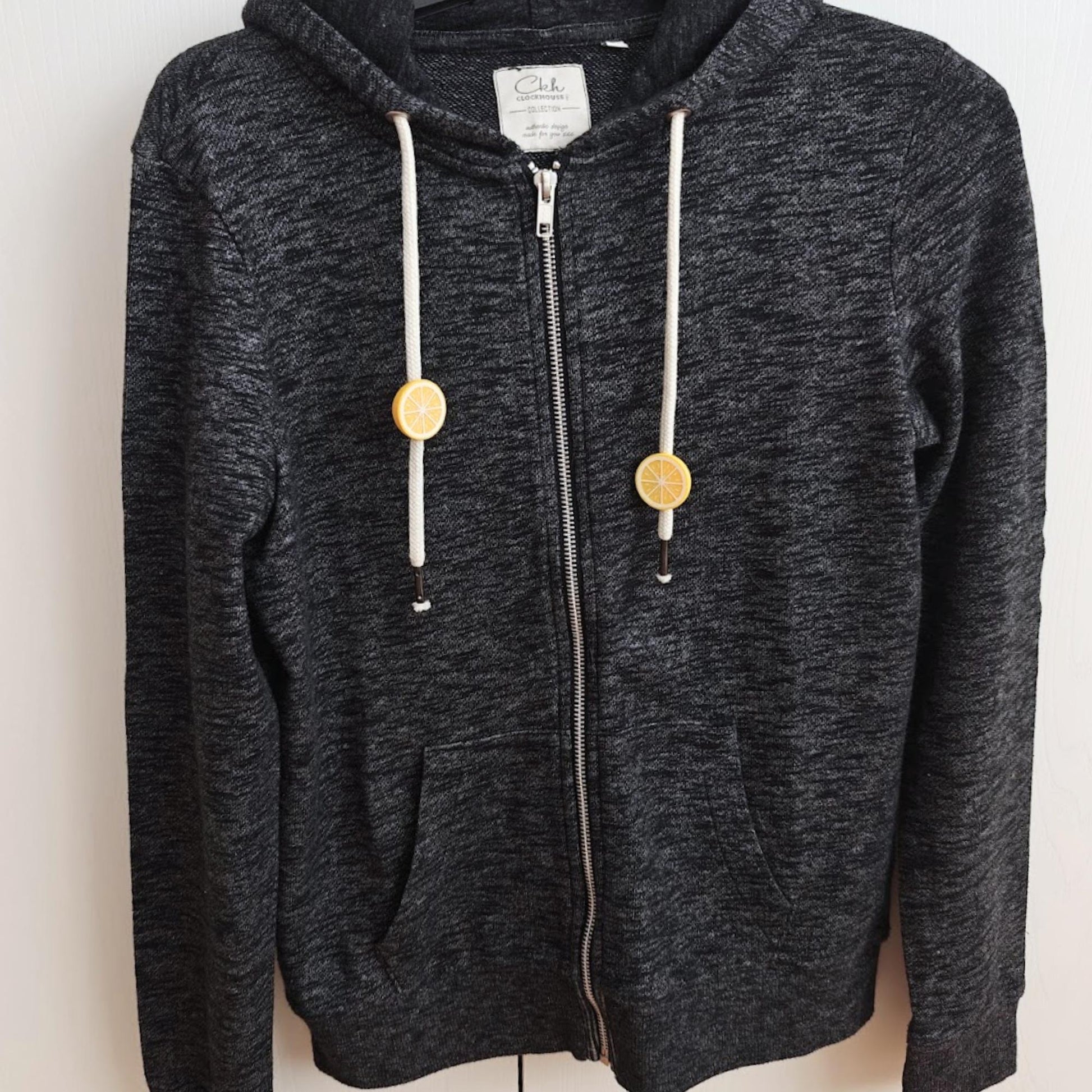 Dark gray zip hoodie with small yellow citrus drawstring charms on the front cords.