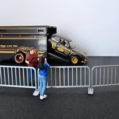 1:64 scale galvanized-style barricades placed in front of a black diecast vehicle and small model figures.