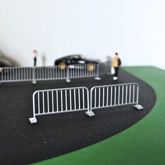 Miniature metal crowd control barricades arranged on a 1:64 scale road diorama with a black diecast car in the background.