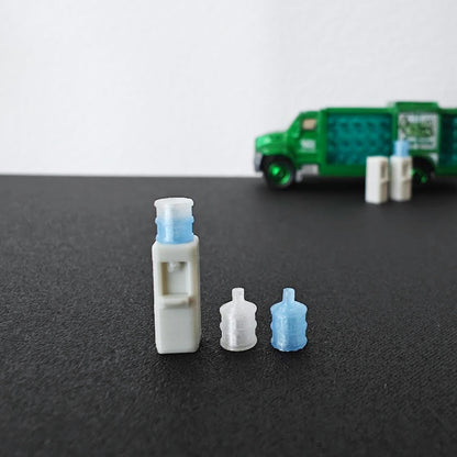 Small 3D printed water dispenser and bottle accessories with a green delivery truck blurred in the background.
