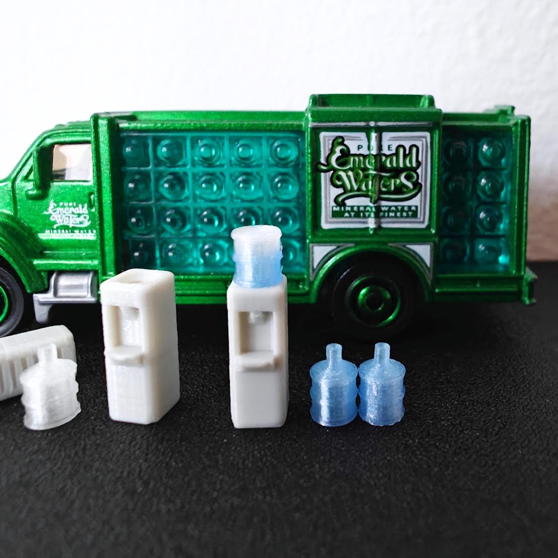 1:64 scale water dispenser accessories arranged in front of a green bottled water delivery truck for diecast scenes.