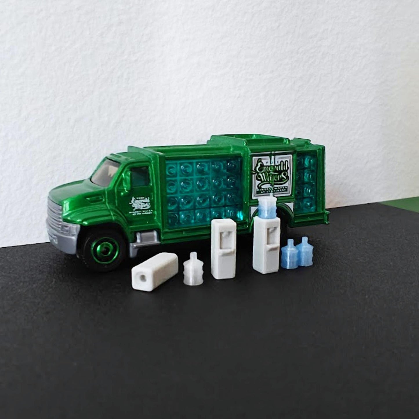 1:64 scale miniature water dispenser set with blue water bottles displayed in front of a green diecast delivery truck.