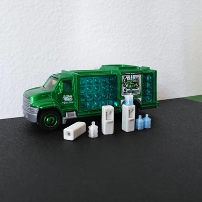 1:64 scale miniature water dispenser set with blue water bottles displayed in front of a green diecast delivery truck.