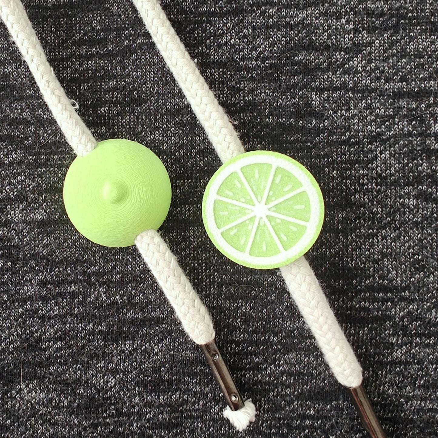 Lime green half-fruit drawstring charms on white hoodie cords, close-up view on dark gray fabric.