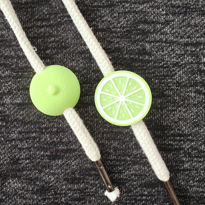 Lime green half-fruit drawstring charms on white hoodie cords, close-up view on dark gray fabric.