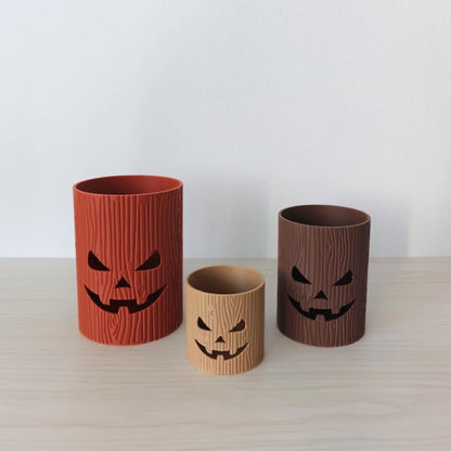 Three spooky tree stump jack-o’-lantern pots in different sizes and colors.