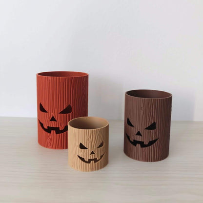 Set of three 3D printed tree stump jack-o’-lantern trinket holders in terracotta, dark brown, and light brown.