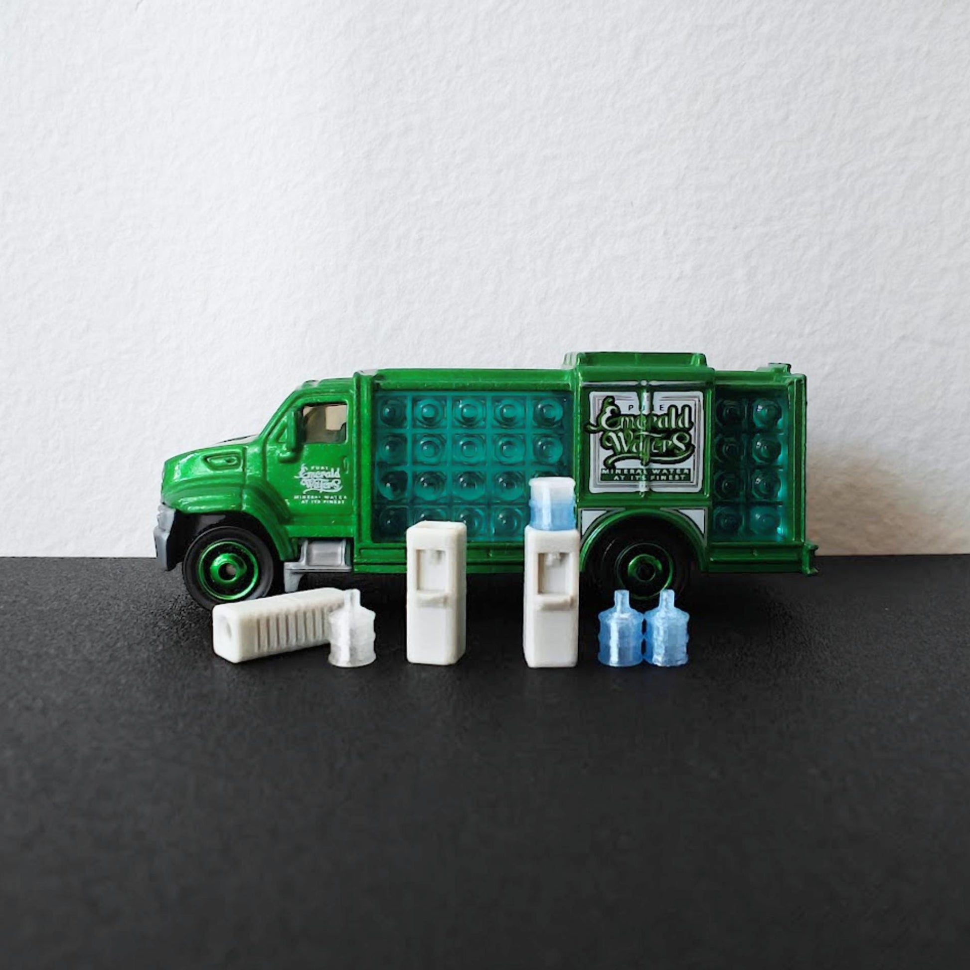 1:64 scale miniature water dispenser set with blue water bottles displayed in front of a green diecast delivery truck.