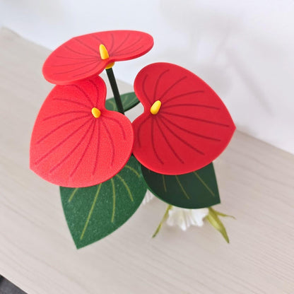 Red Anthurium coaster plant with bright red leaf-shaped coasters and green leaves in a small pot.