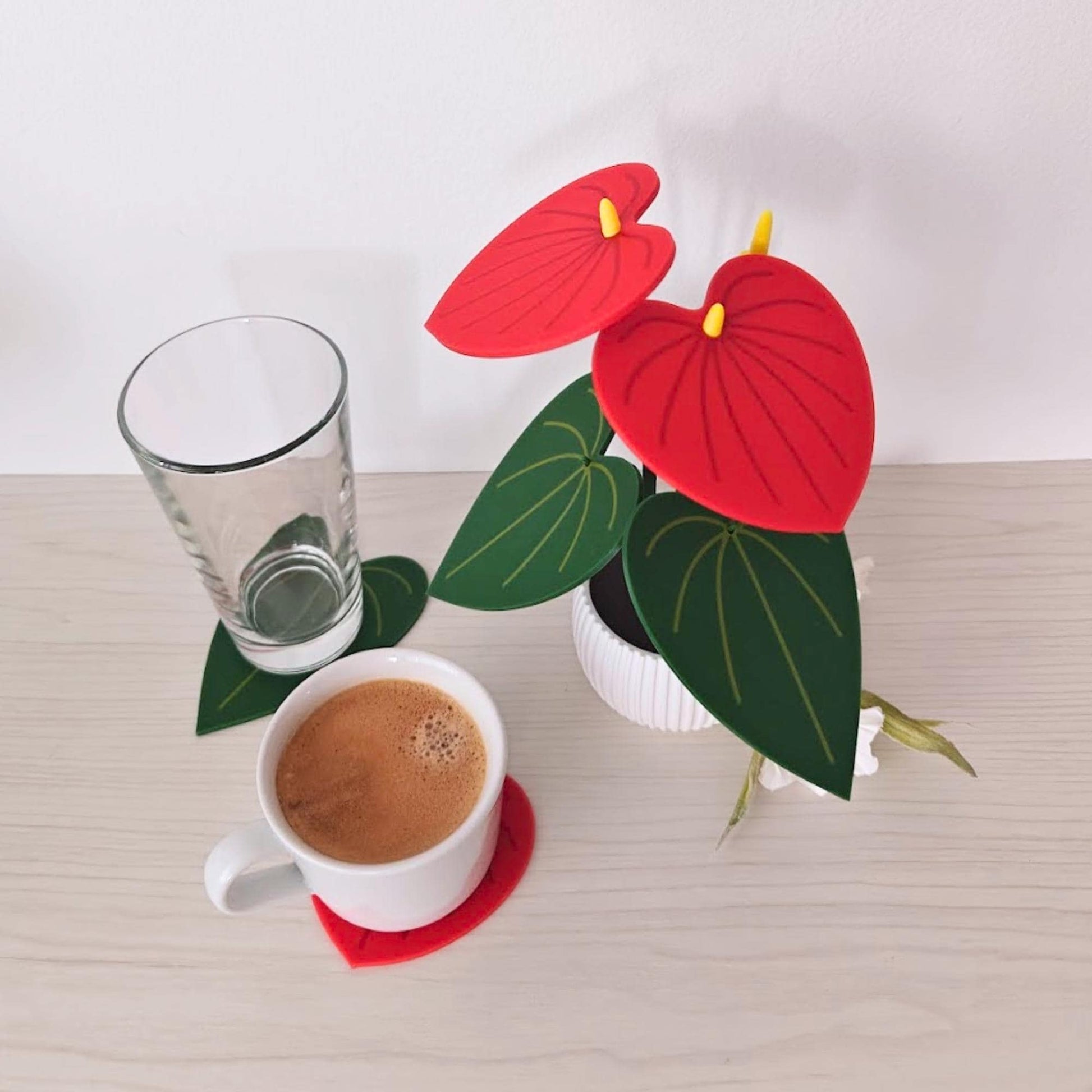 Red Anthurium coaster plant shown with a glass and coffee cup, demonstrating the coaster set in use.
