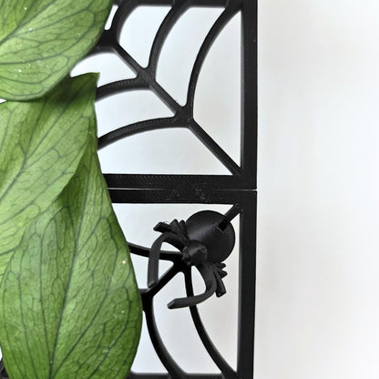 Close-up of green plant leaves climbing through the black spiderweb trellis.