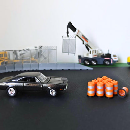 Miniature orange traffic barrels beside a black diecast car and scale construction equipment.