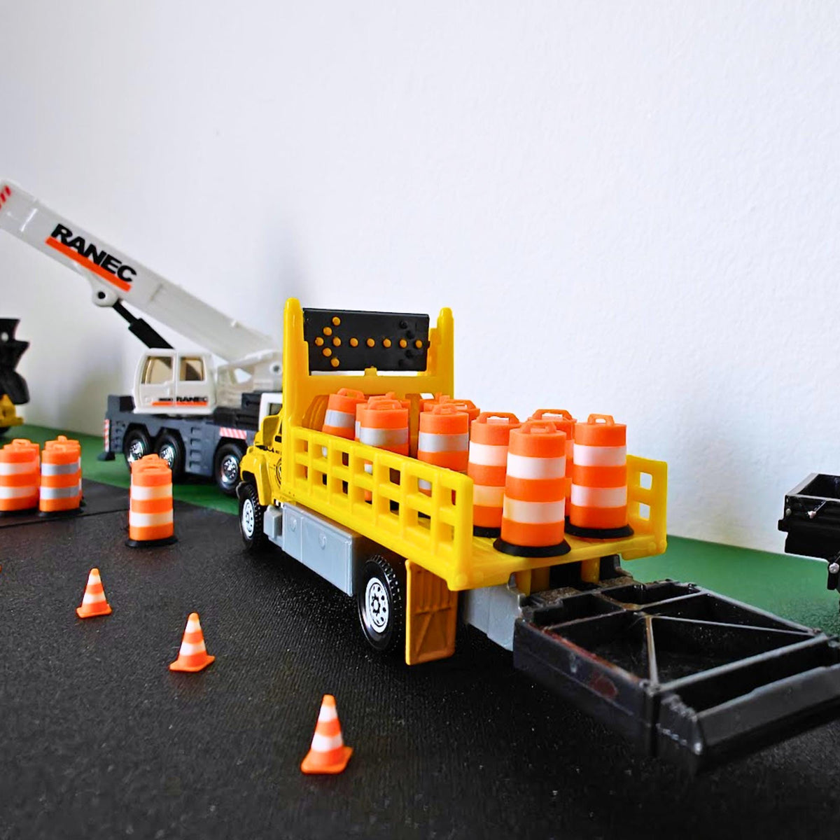 Yellow model construction truck carrying miniature orange traffic barrels with white bands.