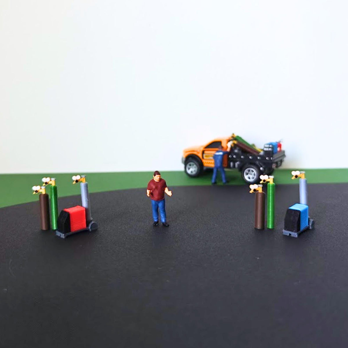 Red and blue miniature welding sets displayed with a scale figure and model pickup truck for size reference.