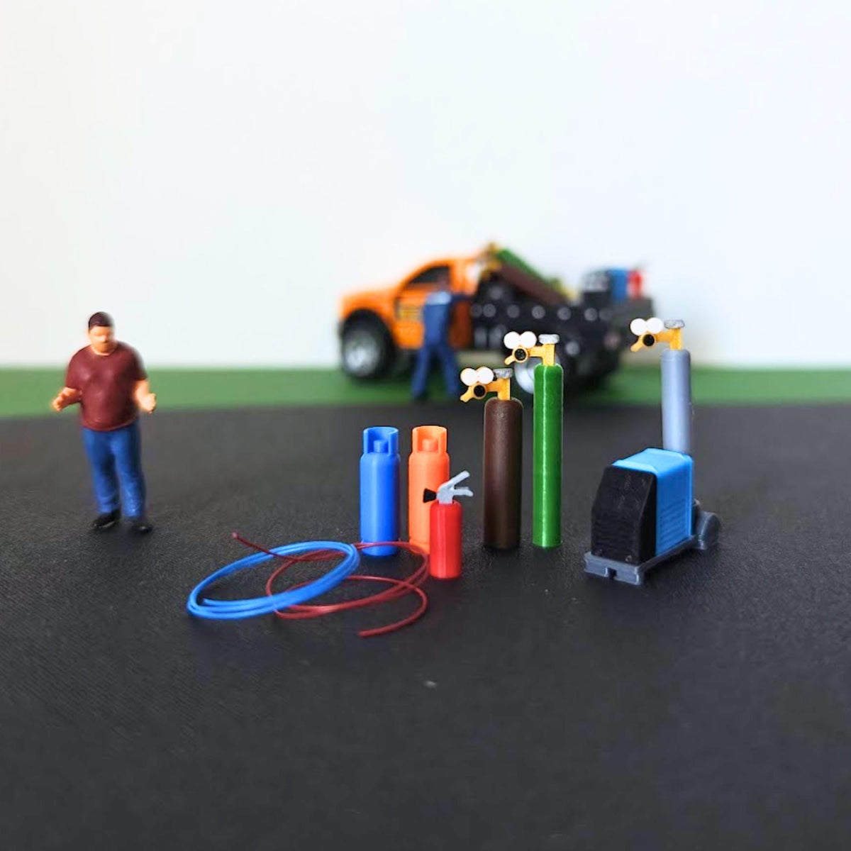 Miniature workshop utility set with gas cylinders, welding machine, fire extinguisher and red and blue hoses in a 1:64 scale diorama.