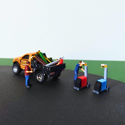 Model pickup truck carrying miniature gas cylinders beside red and blue welding machines and scale figures.