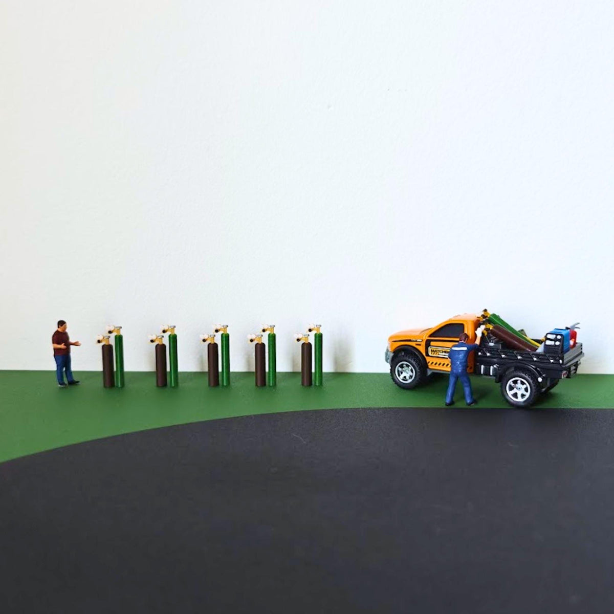 Ten miniature oxy-acetylene cylinders arranged beside a scale figure and orange model pickup truck.