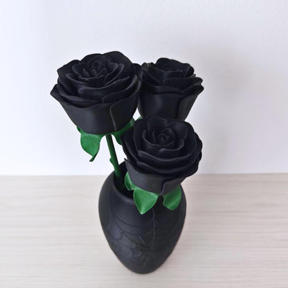 Close-up of three black artificial roses arranged inside a matte black vase with an embossed spiderweb design.