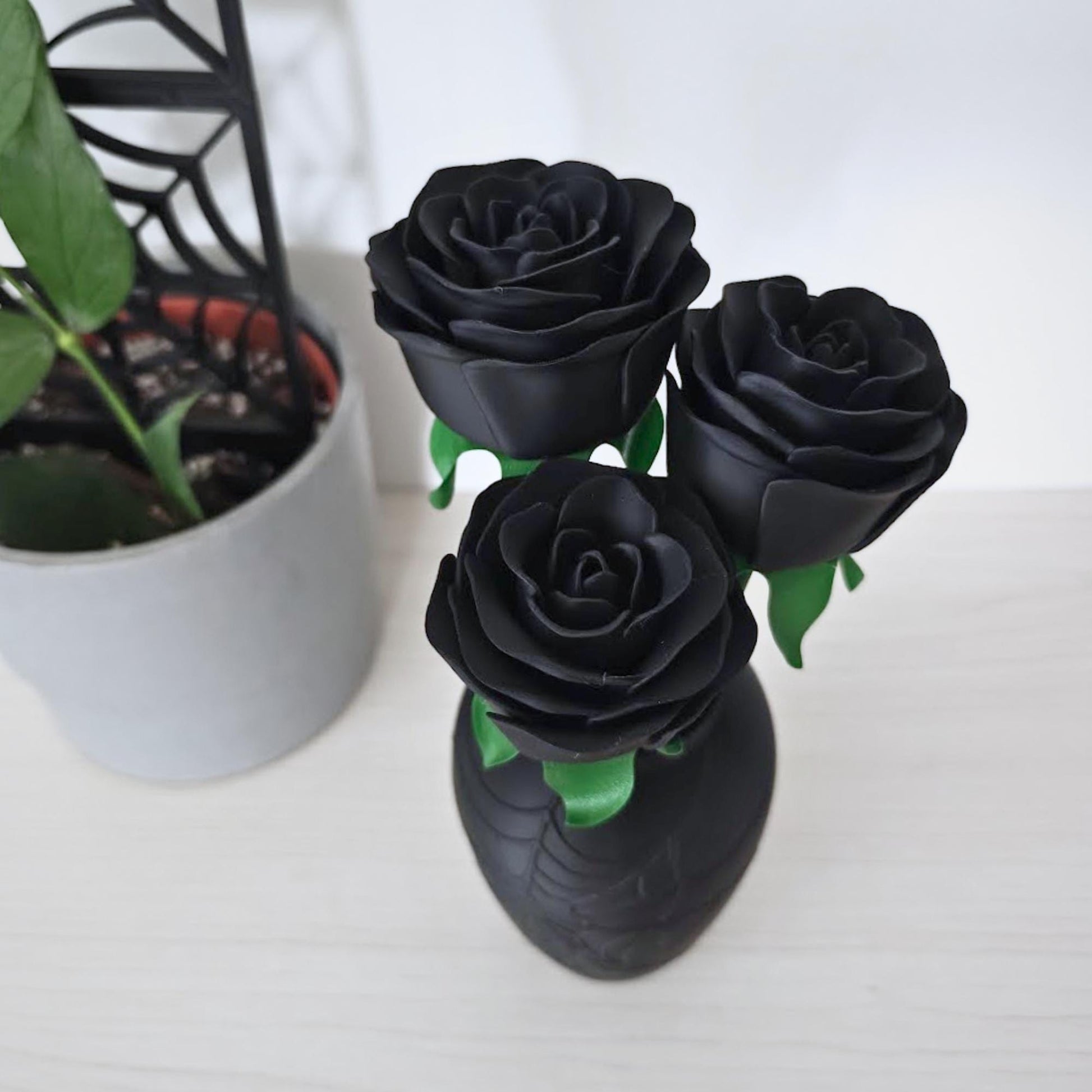 Three black roses arranged in the spiderweb vase, photographed from slightly above beside a grey plant pot.