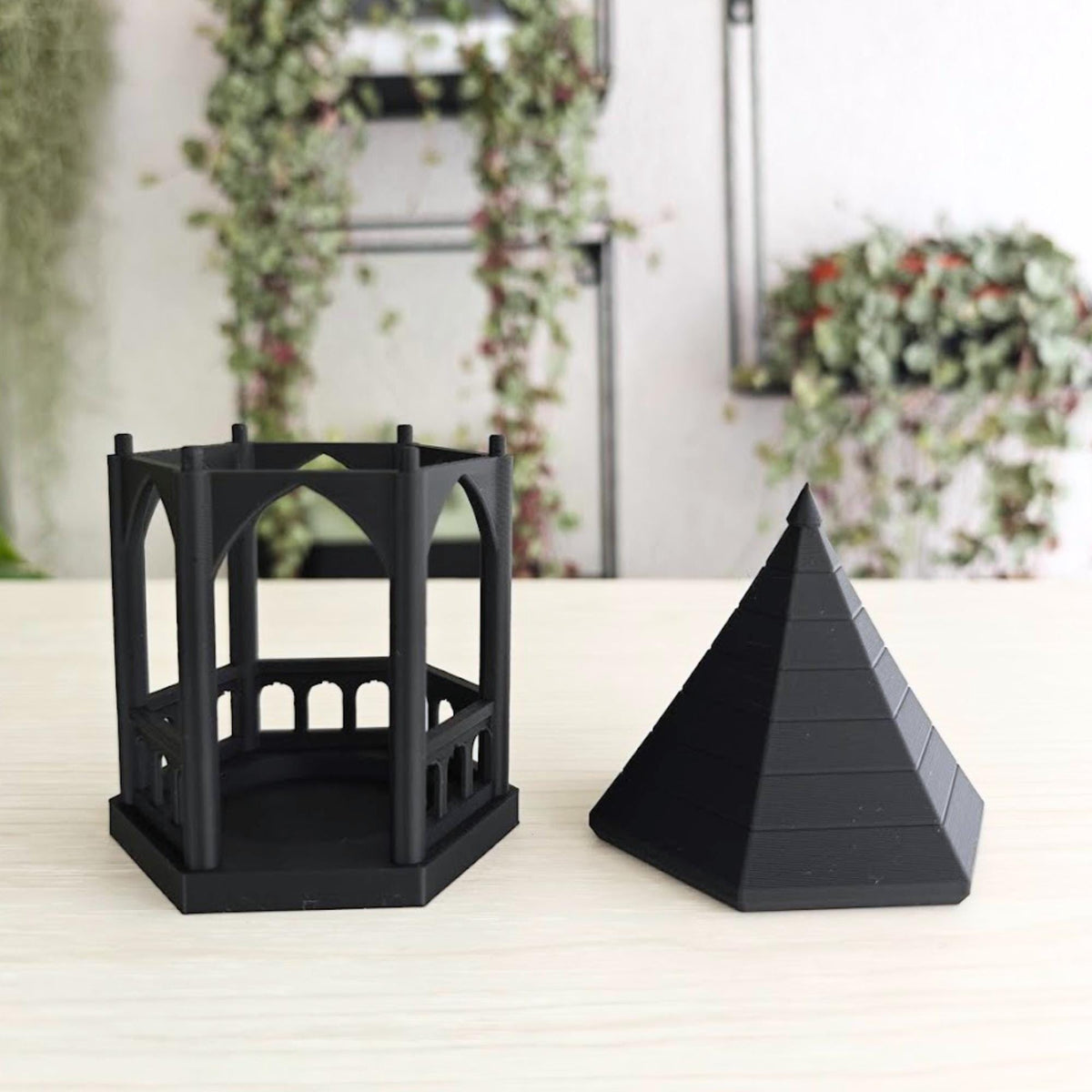 Detached Roof: A black gothic gazebo tealight holder with its pointed, tiered roof removed and placed next to the hexagonal arched base to show how to insert a tealight.