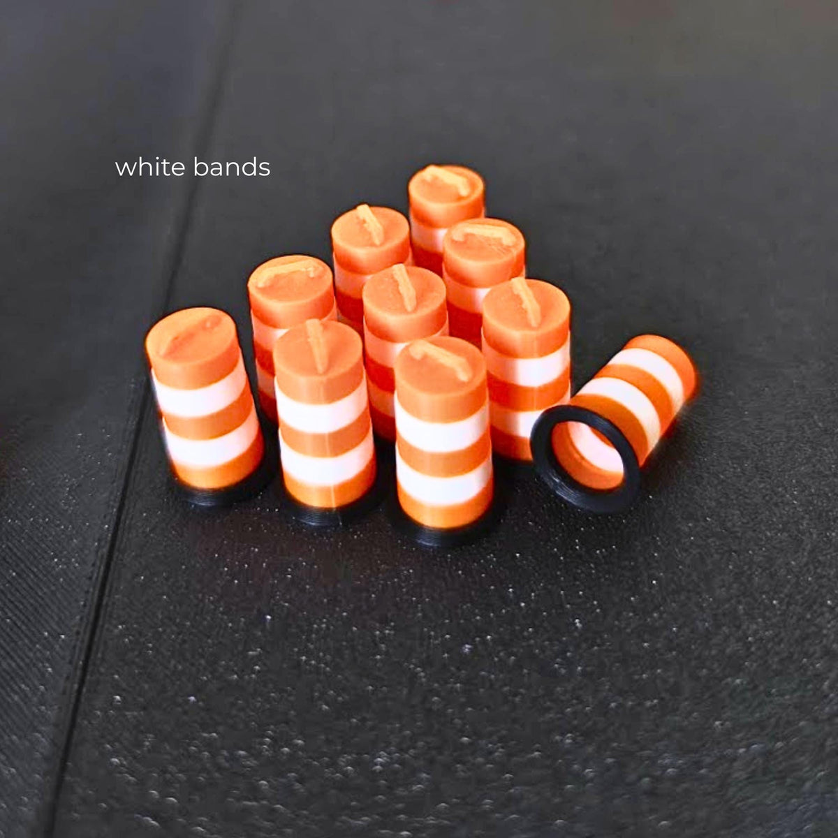 Ten miniature orange traffic barrels with white bands and black bases on a dark background.