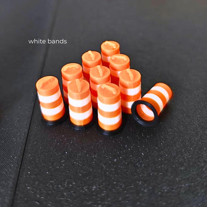 Ten miniature orange traffic barrels with white bands and black bases on a dark background.