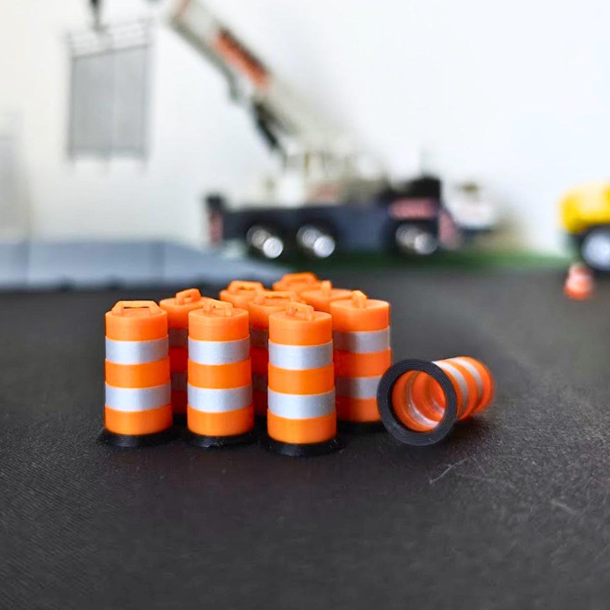 Set of miniature orange traffic barrels with metallic silver reflective bands beside model construction vehicles.
