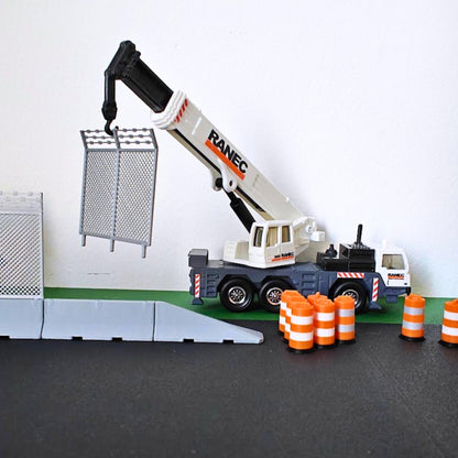 Scale road construction scene with miniature traffic barrels, a crane truck, fencing and road barriers.