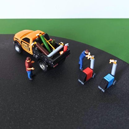 Overhead view of miniature workshop accessories, welding machines, gas cylinders, scale figures and a model pickup truck.