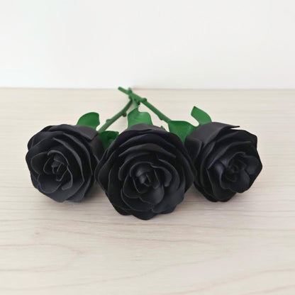 Close-up of three black artificial roses lying side by side on a pale wood surface.