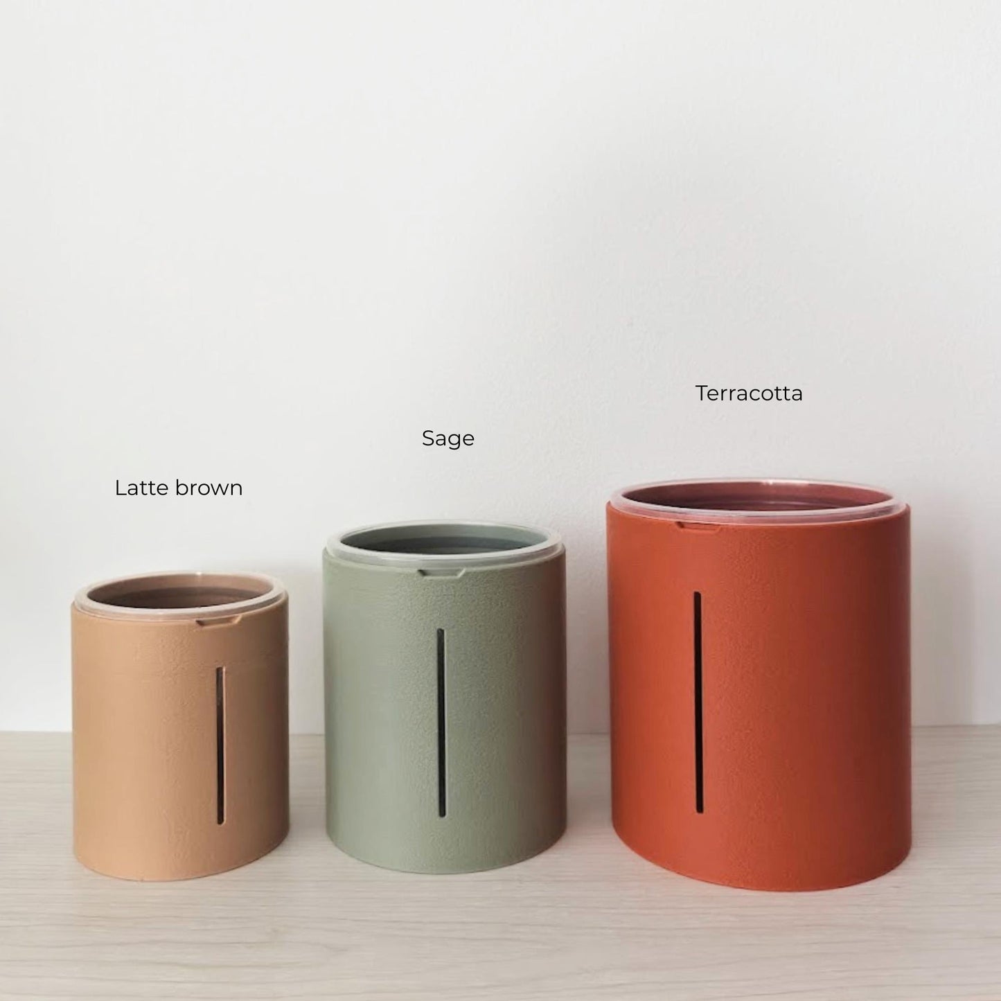 Three textured planter covers in latte brown, sage green and terracotta, shown together on a light wood surface.
