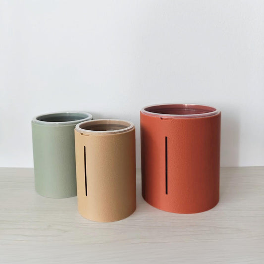 Three textured tall aroid planter covers in sage green, latte brown and terracotta, each with a vertical airflow opening.