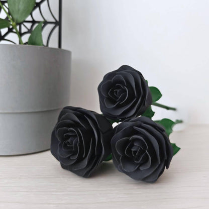 Three detachable black rose heads lying on a pale wooden surface with green stems visible behind them.