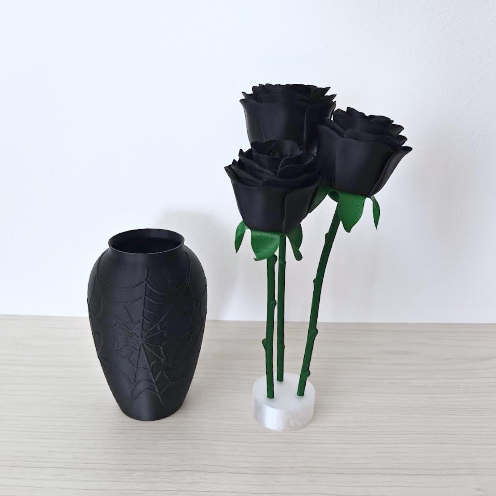 Black spiderweb vase displayed beside three faux roses supported upright outside the vase.