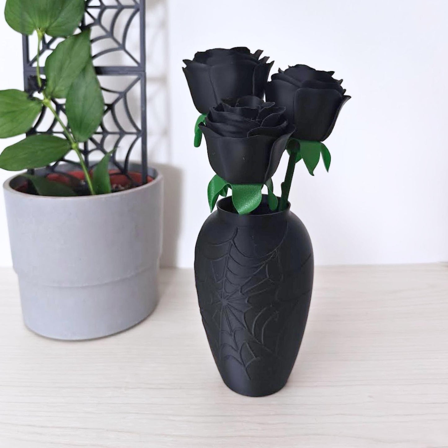 Front view of three black faux roses displayed in a matte black vase with an embossed cobweb pattern.