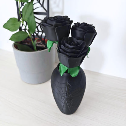 Angled view of the black rose bouquet in its spiderweb vase beside a green houseplant.