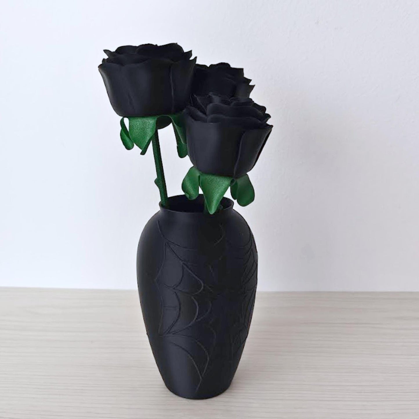 Side view of three black artificial roses arranged in the black cobweb vase against a white background.