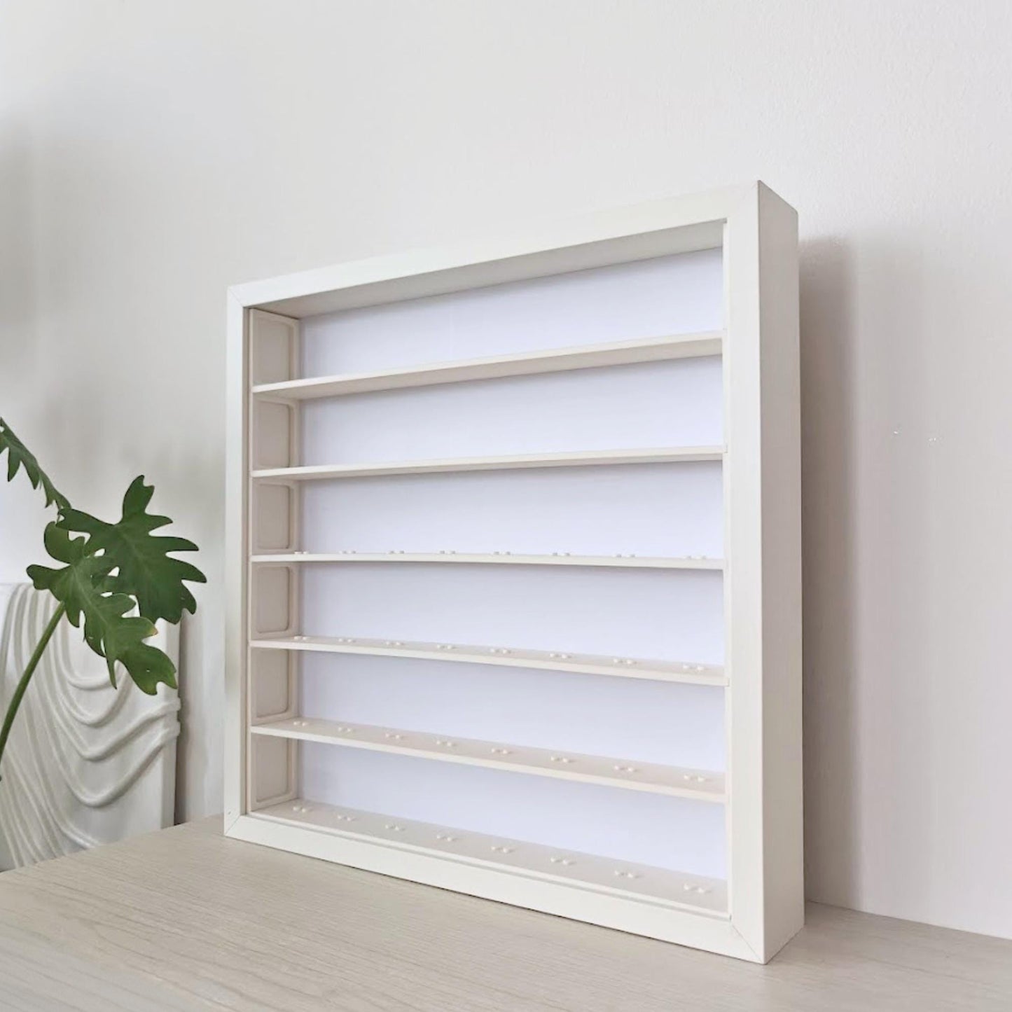 Angled view of the empty white display grid inside a SANNAHED frame, shown beside a houseplant.