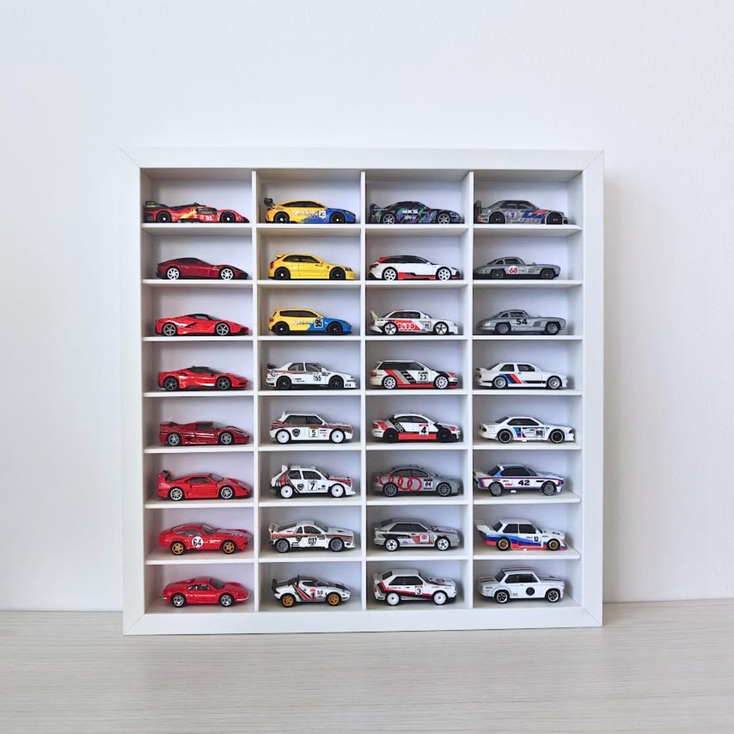 Front view of a white IKEA SANNAHED 35 × 35 cm frame with a 32-compartment grid displaying colorful 1:64-scale diecast cars.
