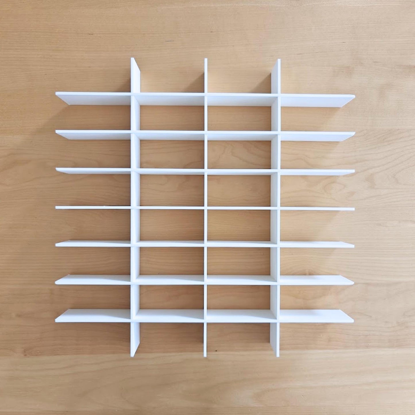 Fully assembled white interlocking display grid shown outside the frame on a wooden surface.